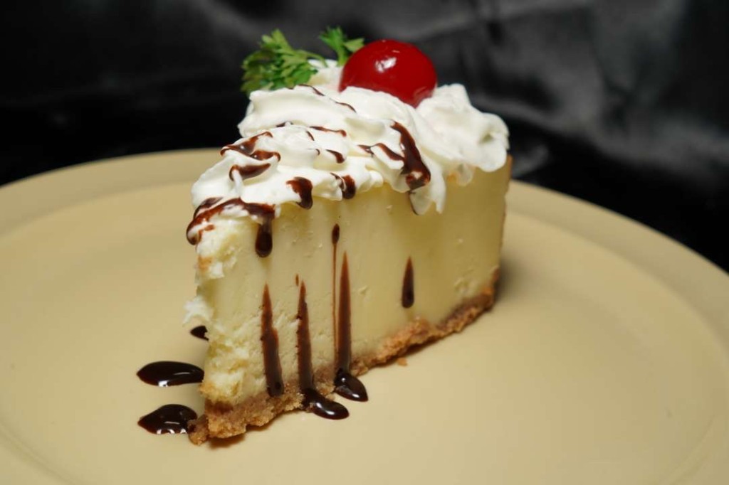 A slice of cheesecake with whipped cream, chocolate, and a cherry