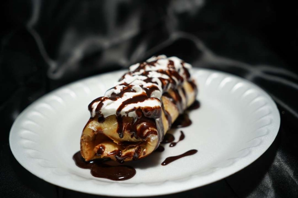 A rolled dessert with whipped cream and chocolate sauce