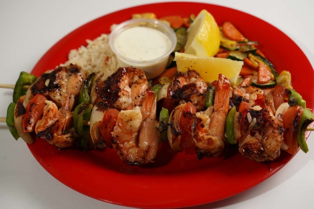 Grilled shrimp skewers with rice, lemon, and vegetables on a red plate