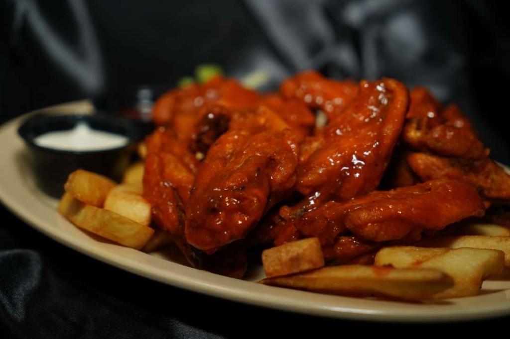 A plate of sauced wings with fries and ranch